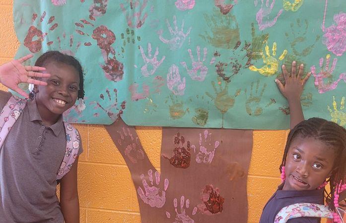  two girls standing in front of a tree with painted hand prints